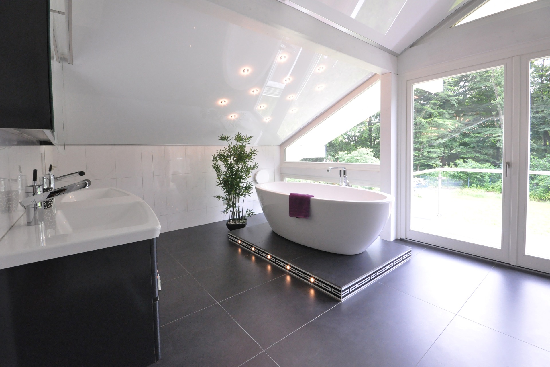 Berse Sanitär Ein modernes Badezimmer mit freistehender Badewanne, großem Waschtisch und Panoramafenster in einen Garten.