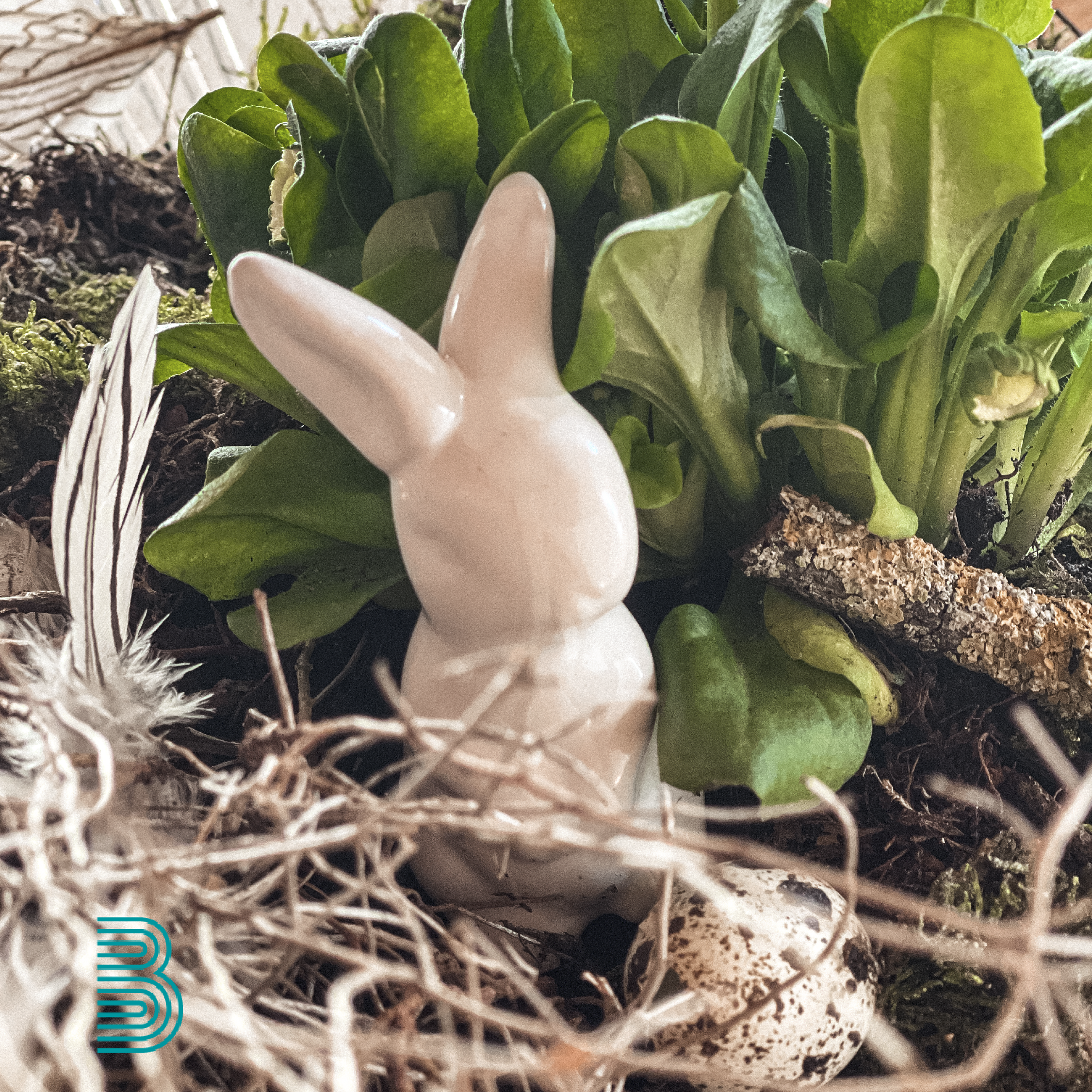 2023_04_ostern_kachel Eine DEkoosterhase steht inmitten österlichem Gesteck.