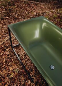 Eine grüne Badewanne steht auf Herbstlaub. 