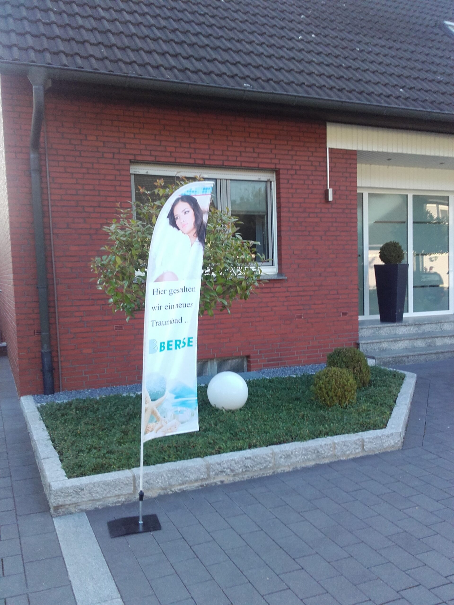 Eine Beachflag von der Berse GmbH steht vor einer Haustür, um zu zeigen, dass hier ein neues Bad entsteht.