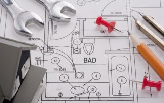 Ein Bauplan für ein Badezimmer mit Bleistift, Reiszwecken und Schraubschlüsseln darauf.