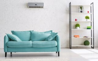 Eine türkisfarbene Couch steht unter einem Klimagerät in einem Wohnraum.