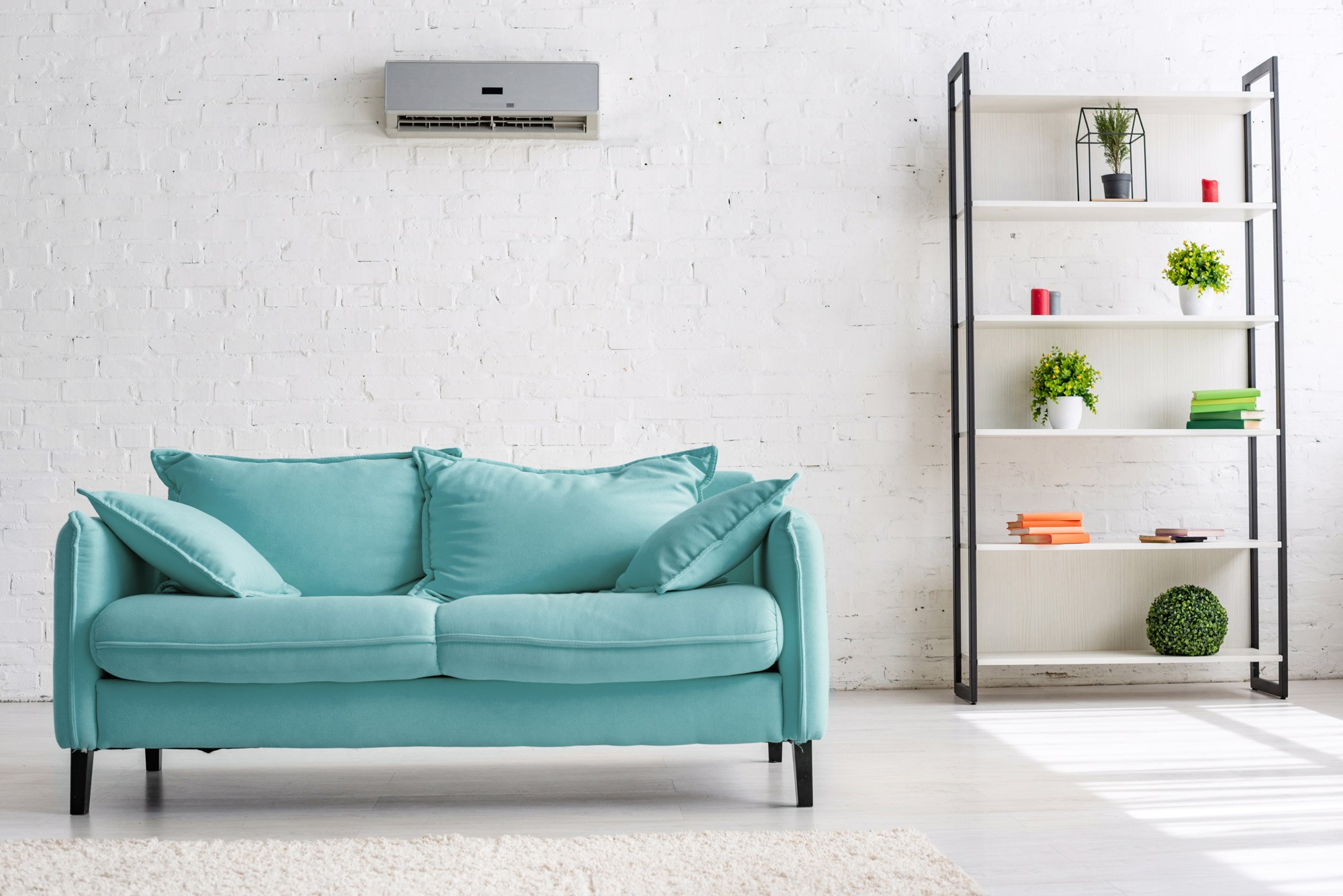 foto_ta_rkisessofa_klein Eine türkisfarbene Couch steht unter einem Klimagerät in einem Wohnraum.