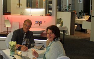Ulrich und Carme Berse sitzen an einem Esstisch inmitten einer Badausstellung.