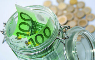 Zwei Hundert-Euro-Scheine stecken in einem Einmachglas. Dahinter liegt Münzgeld.