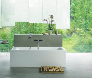 Eine Badewanne steht vor einem lichtdurchfluteten großen Fenster mit Vorhängen. 