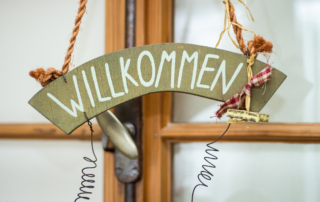 Ein Schild mit der Aufschrift "Willkommen" hängt an einer Tür.