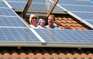Eine dreiköpfige Familie schaut aus einem Dachflächenfenster auf Solarplatten.