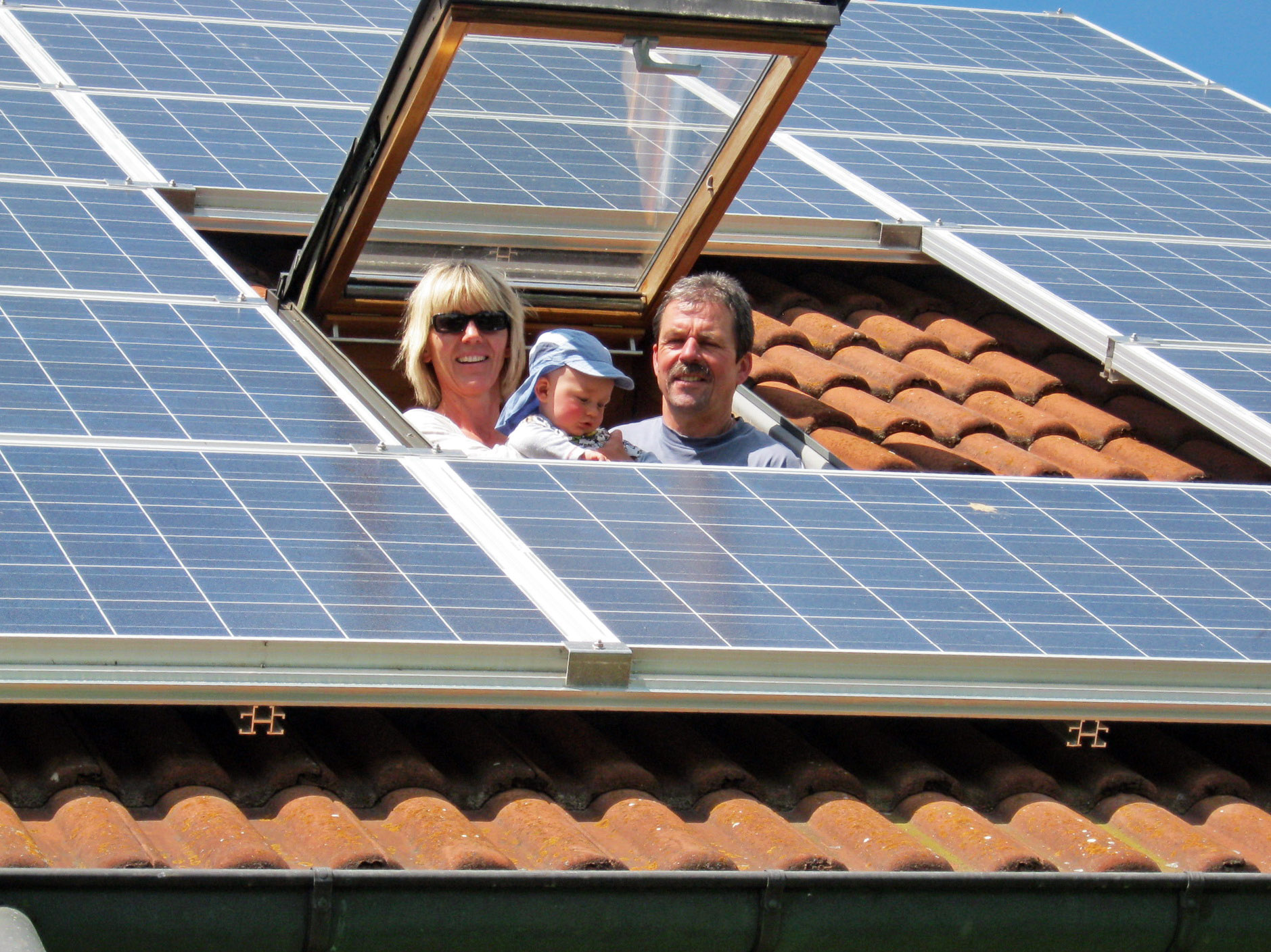 solarstrom_familie_dachfenster Eine dreiköpfige Familie schaut aus einem Dachflächenfenster auf Solarplatten.