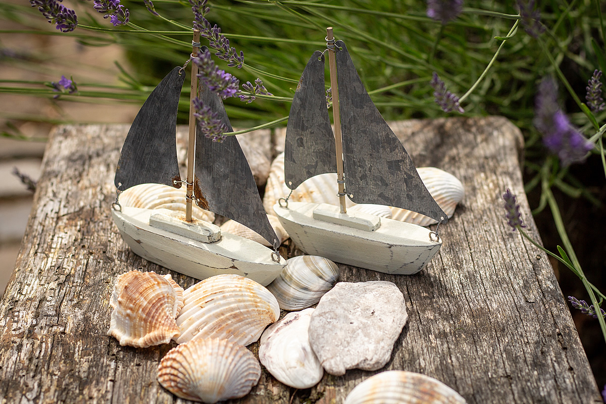 sommer Zwei Miniatur-Segelbote aus Holz stehen zur Dekoration auf einem Tisch, Muscheln liegen daneben.