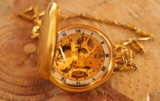 Eine goldene Taschenuhr liegt aufgeklappt auf einem Tisch und das Ziffernblatt sowie die dahinterliegende Mechanik sind zu sehen.
